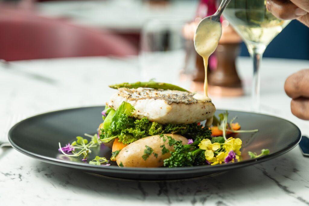 Gourmet fish dish elegantly presented with fresh vegetables and sauce, set on a luxurious marble table in a fine dining setting.