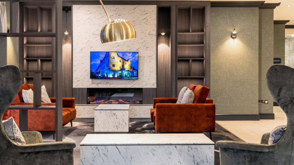 Stylish hotel lounge with plush seating, a modern fireplace, marble decor, and warm lighting, offering a cosy atmosphere.