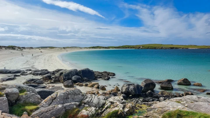 Stunning coastal view of white sandy beach and turquoise sea, with rocky foreground, ideal for relaxed seaside strolls.