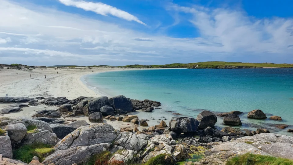 Stunning coastal view of white sandy beach and turquoise sea, with rocky foreground, ideal for relaxed seaside strolls.