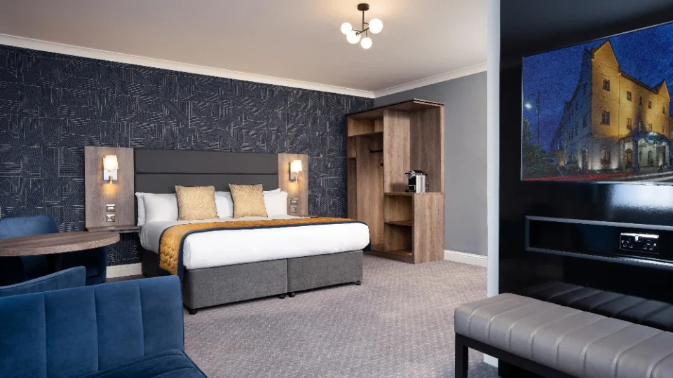 Stylish hotel room with cosy double bed, chic navy sofa, modern lighting, and in-room coffee maker. Perfect for relaxation.