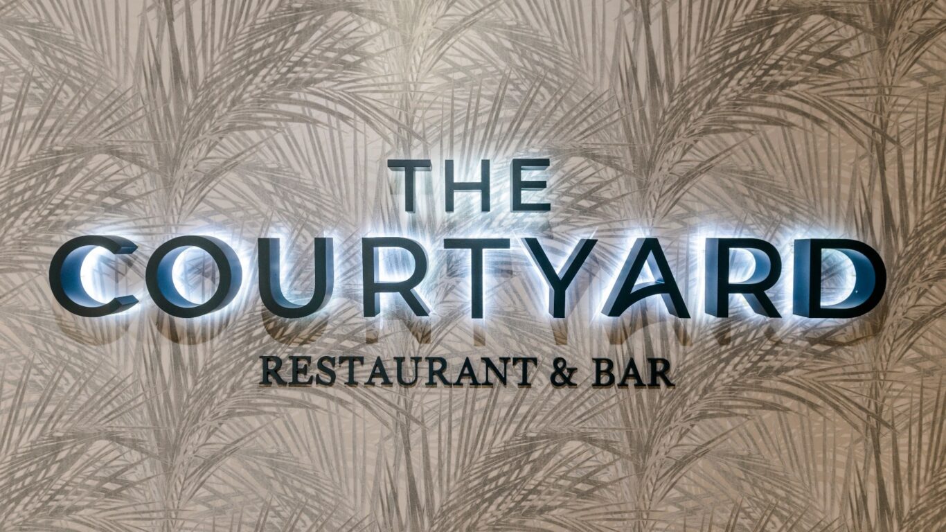 Elegant Courtyard Restaurant & Bar sign with stylish palm-patterned background, inviting ambiance for guests.