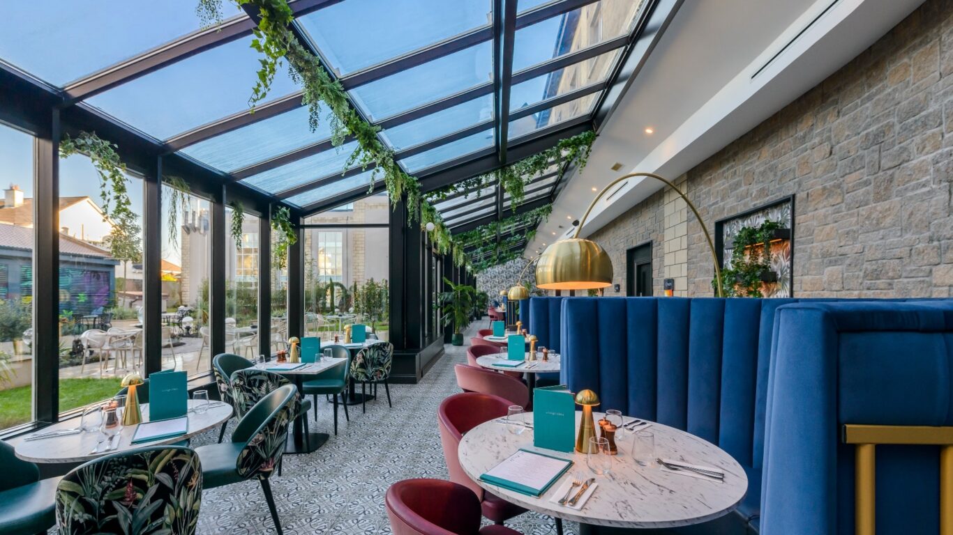 Sunlit conservatory dining area with plush seating, leafy decor, and a garden view for a cosy, inviting hotel experience.