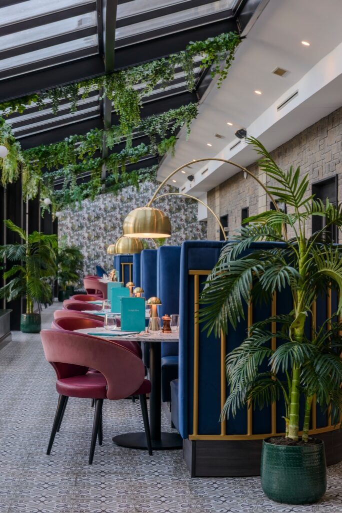Elegant hotel dining area with lush greenery, cosy seating, and ambient lighting, offering a warm and inviting experience.