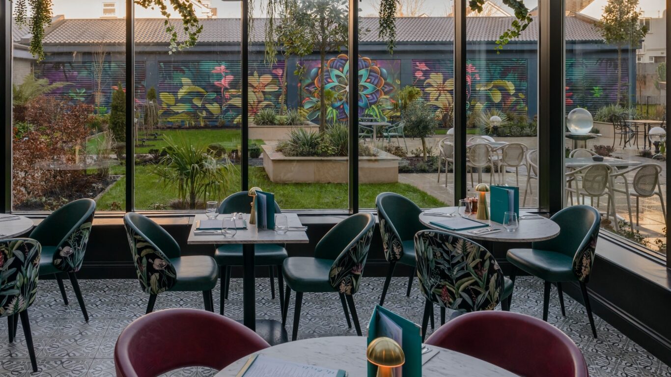 Modern hotel dining area with elegant chairs, colourful mural view, and lush garden, offering a relaxed dining experience.