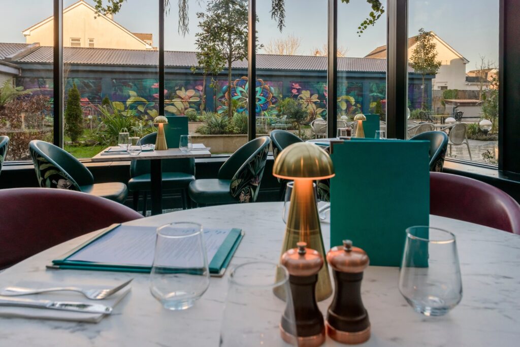 Elegant hotel dining area with garden view, featuring vibrant mural, cosy seating, stylish decor, and ambient lighting.