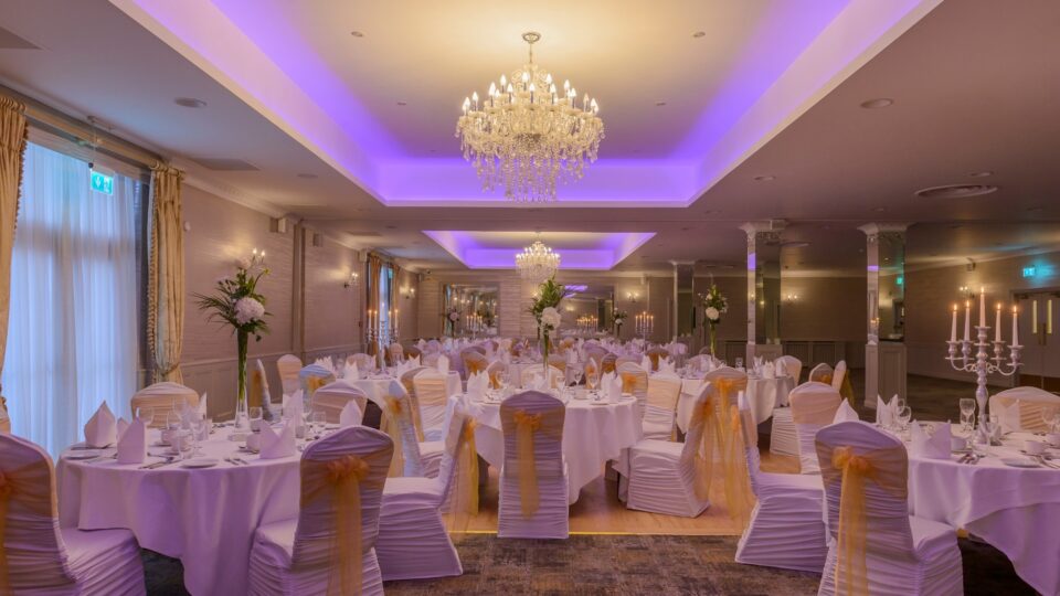 Elegant banquet hall with chandeliers, decorated tables, and ambient lighting, ideal for weddings and events.