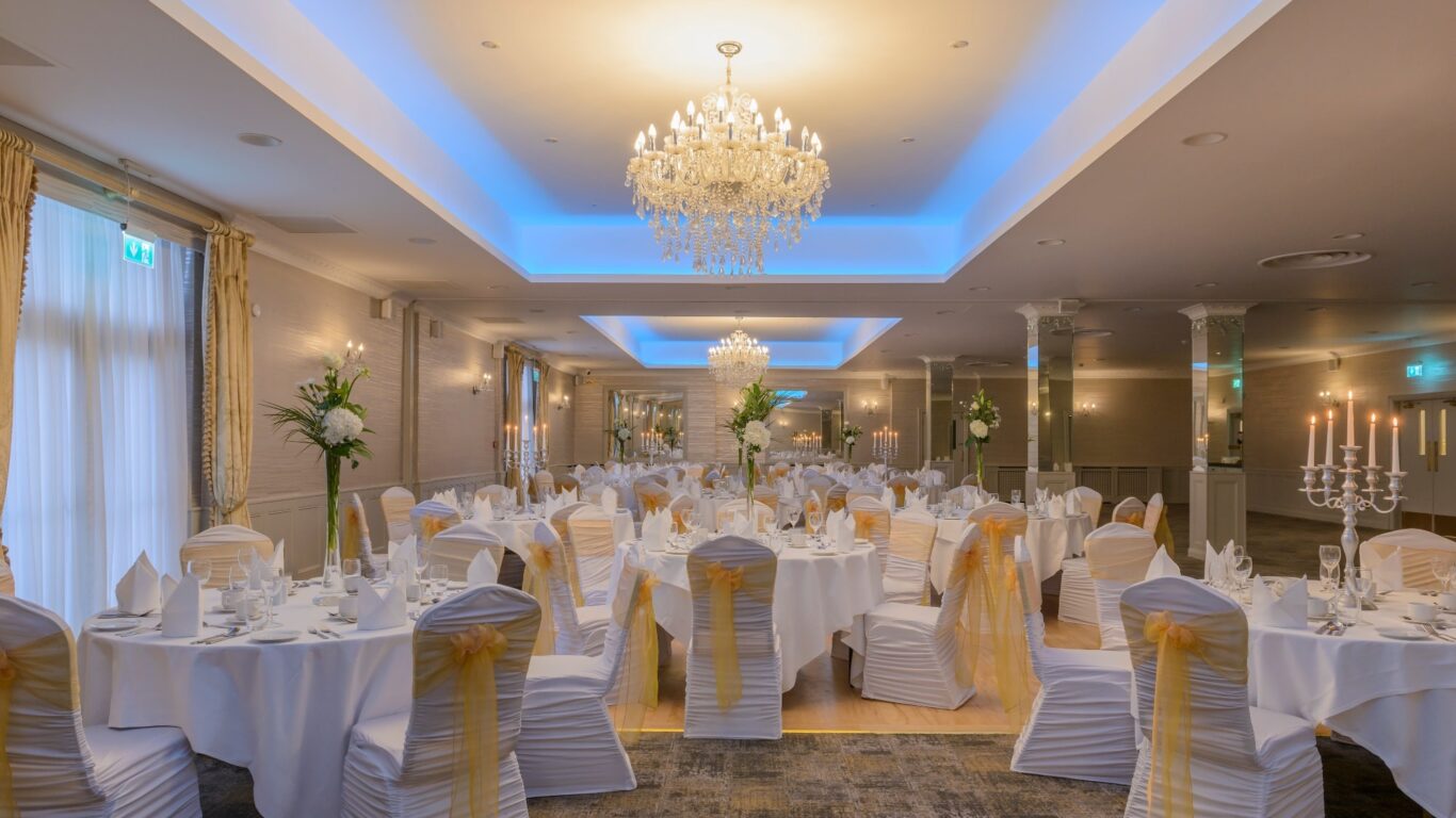 Elegant banquet hall with chandeliers, white-gold decor, and round tables set for a wedding at a luxury hotel.