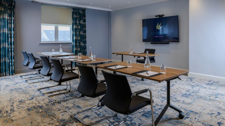 Modern meeting room with stylish chairs, wooden tables, large screen, and natural light decor, ideal for conferences.