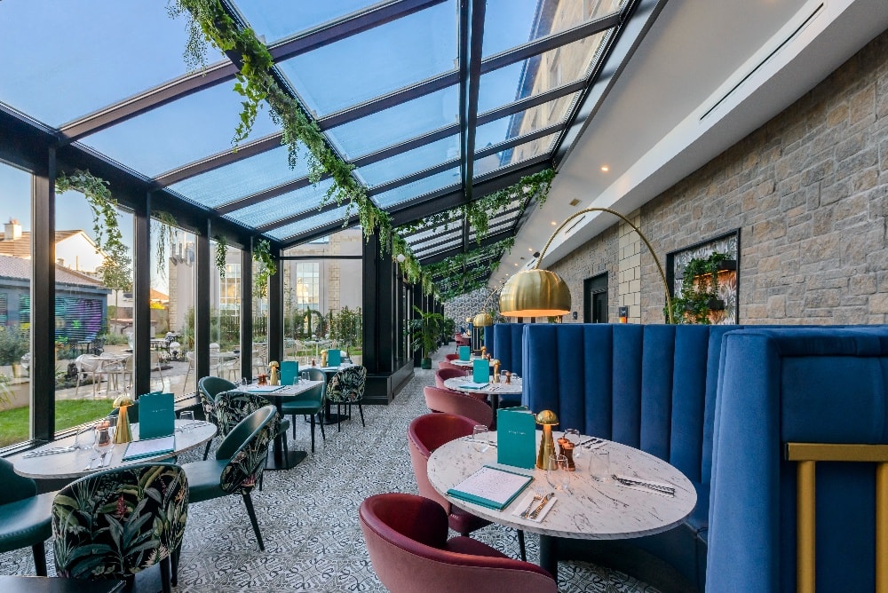 Bright hotel conservatory dining with skylights, elegant seating, lush greenery, perfect for relaxed breakfasts or dinners.