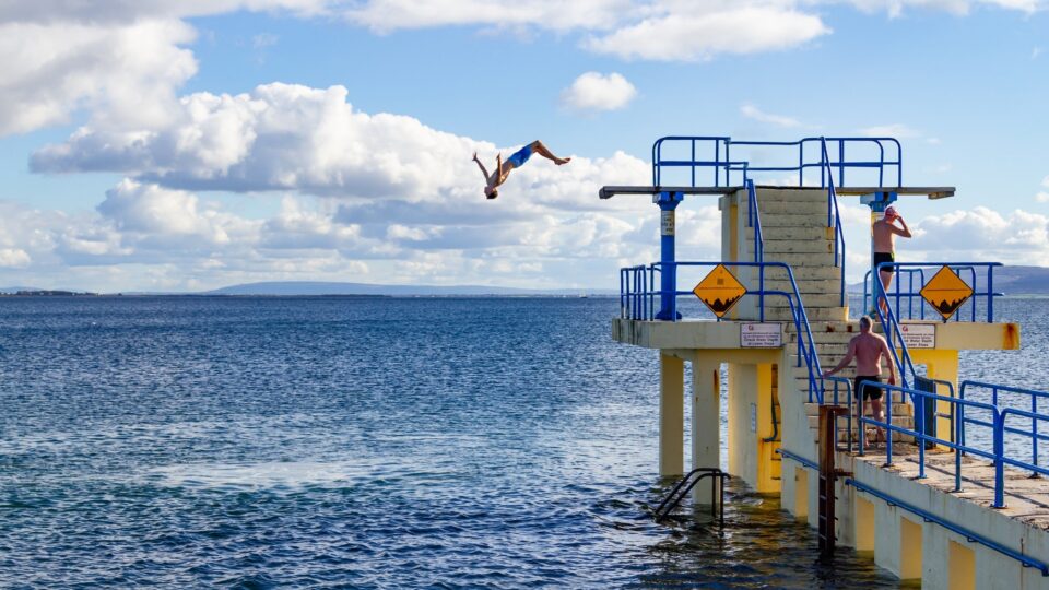Guests diving from a blue and yellow pier into clear waters under a sunny sky, experiencing seaside adventure.