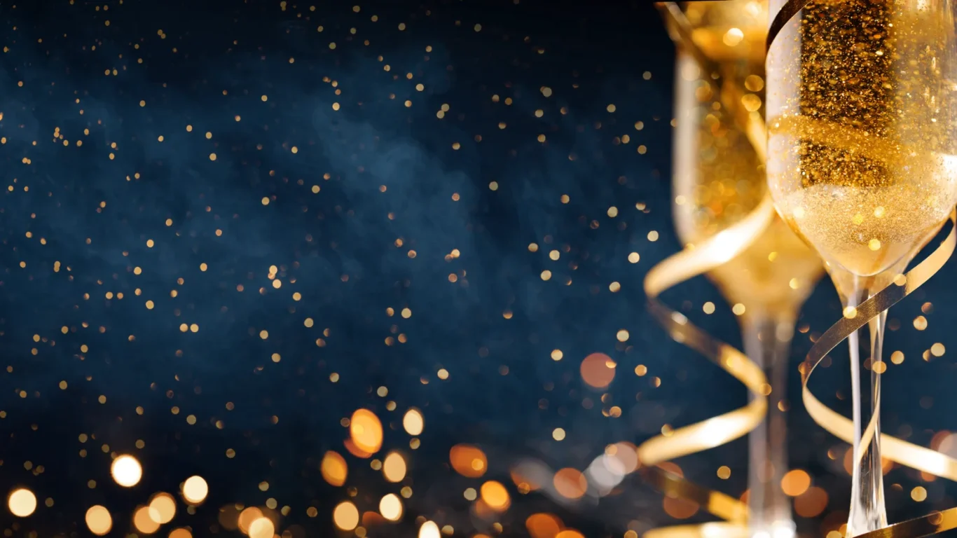 Two champagne glasses with gold ribbons and sparkling bubbles, set against a dark background with scattered golden light bokeh.