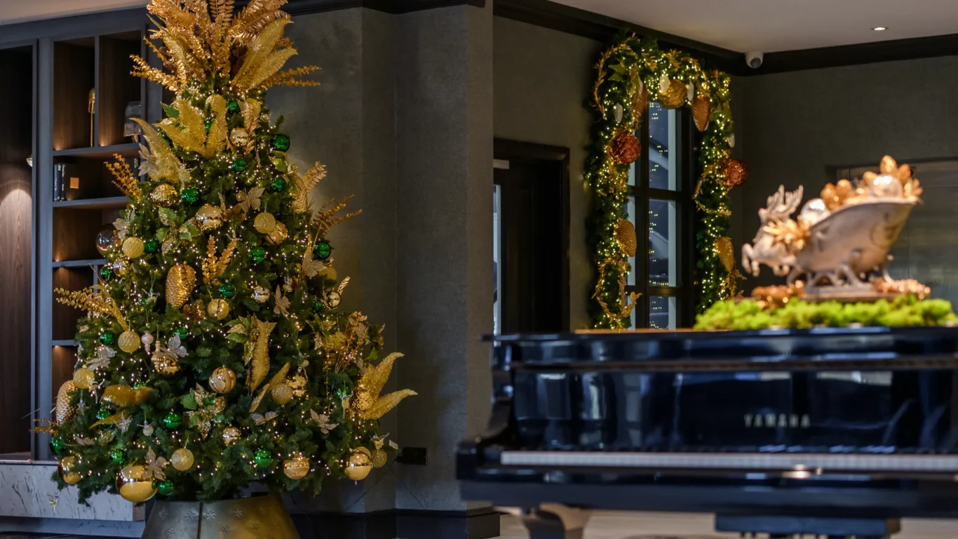 A decorated Christmas tree with gold and green ornaments stands near a doorway adorned with matching garland in a room with a Yamaha grand piano in the foreground.