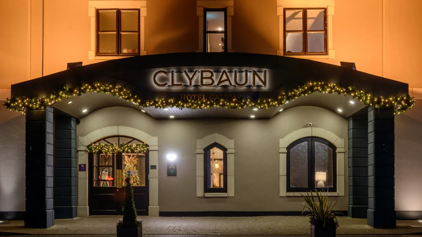 The front entrance of Clybaun Hotel at night, decorated with yellow string lights, with three arched windows and a door.