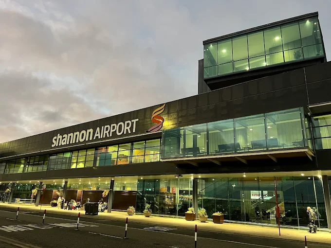 Exterior view of Shannon Airport terminal building at dusk, with large glass windows and illuminated signage visible.
