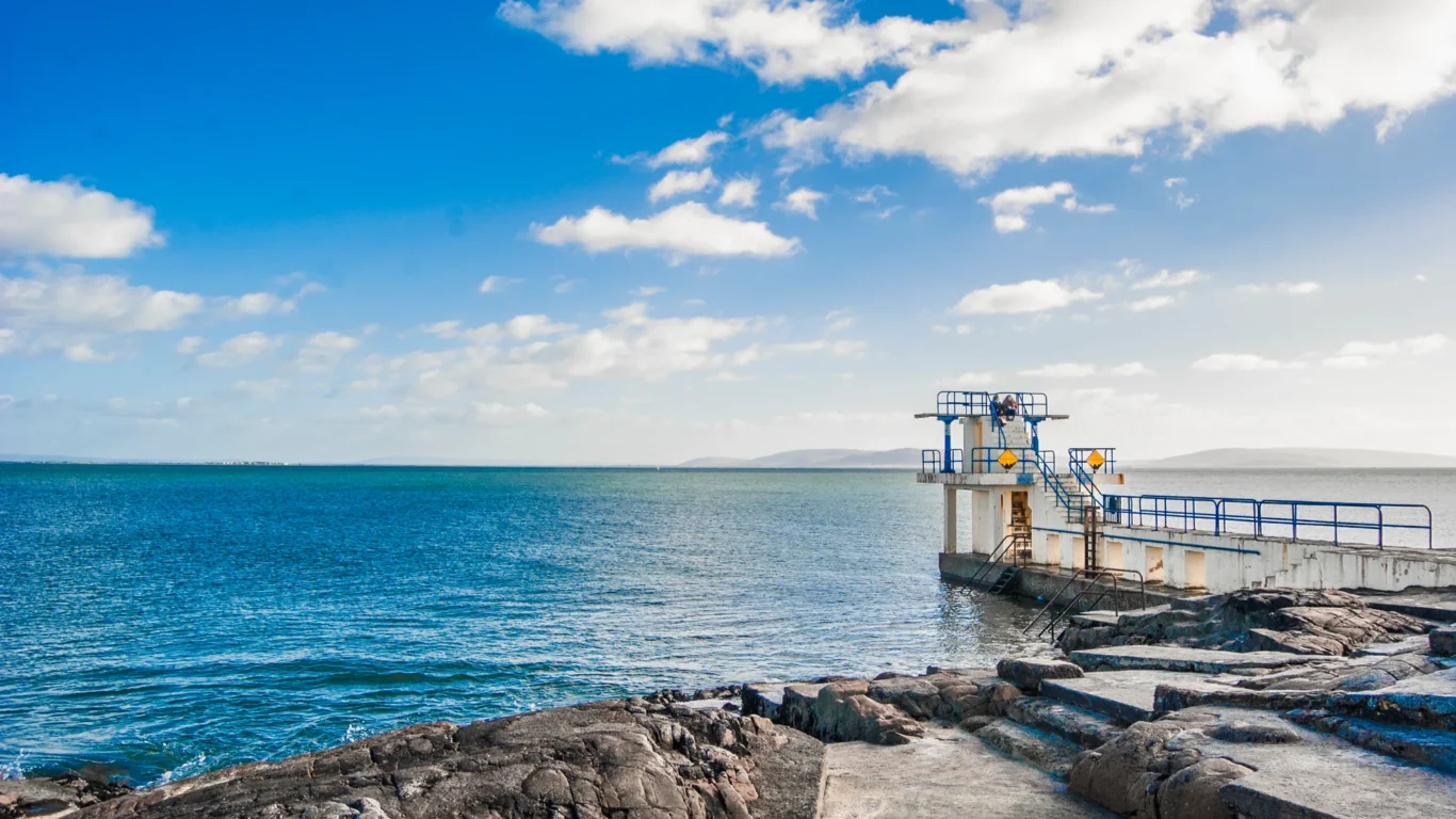 Stunning ocean view from the rocky shore with a diving platform under a sunny blue sky, perfect for seaside relaxation.