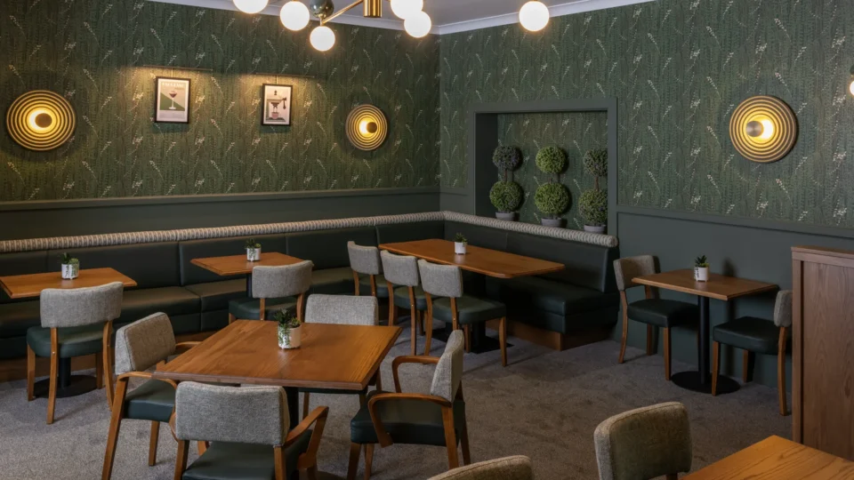 Chic hotel cafe with cosy seating, green wallpaper, modern lighting, and welcoming decor for a relaxing dining experience.