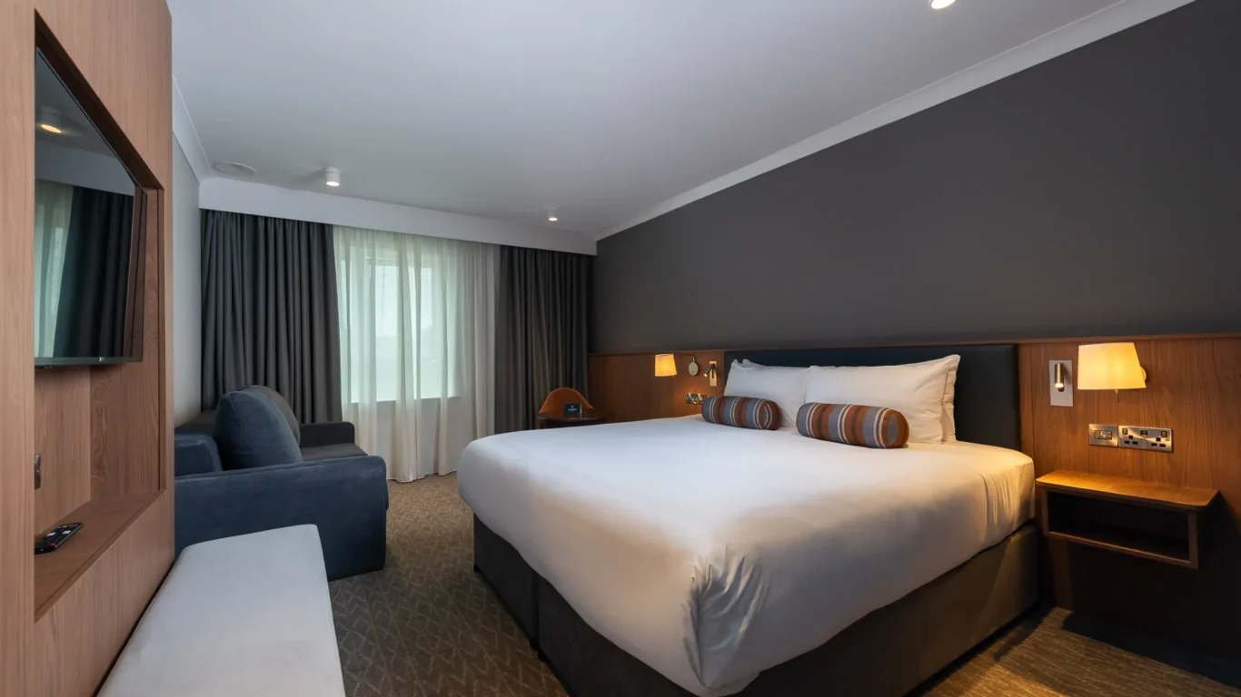 Elegant hotel room with king-sized bed, stylish decor, cosy seating, and ambient lighting, ideal for a relaxing stay.