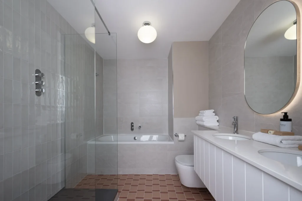 Elegant hotel bathroom with spacious glass shower, tub, double sink, plush towels, and relaxing modern decor.