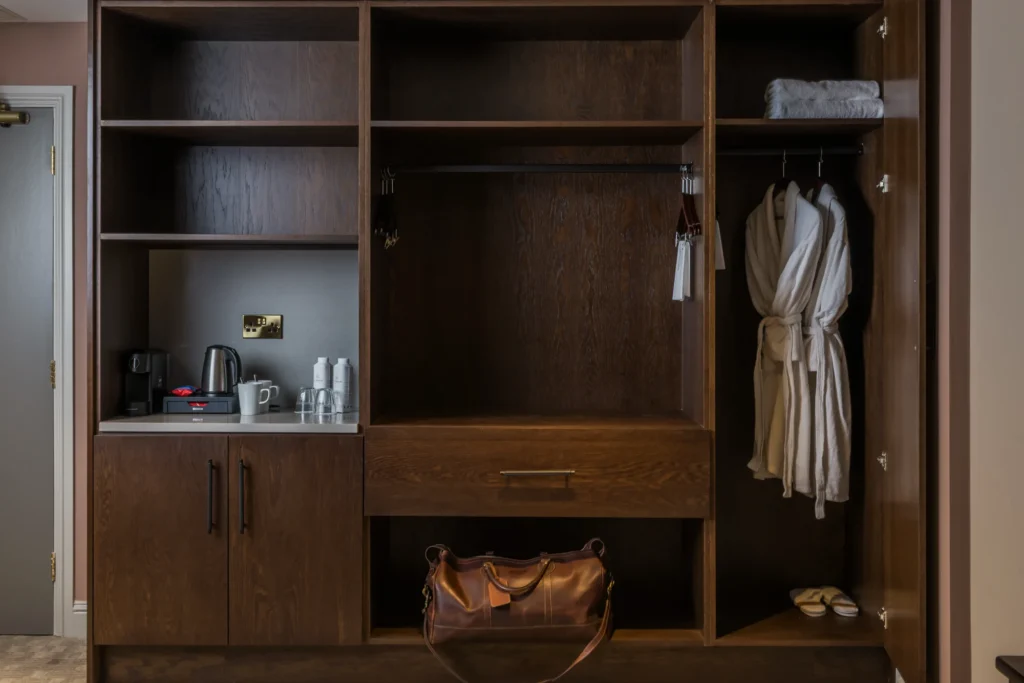 Luxurious wardrobe with cosy robes, leather bag, tea station, and slippers in a stylish hotel room.