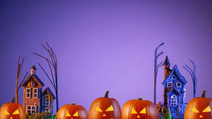 Spooky Halloween scene with glowing pumpkins and haunted houses against a purple sky, perfect for a festive hotel stay.
