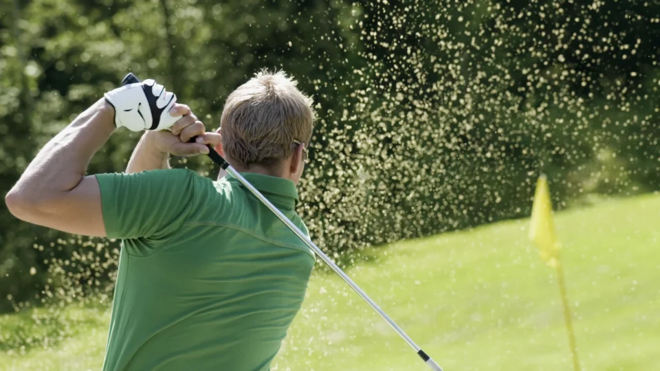 Guest enjoying golf on lush course, swing creating sand splash, hotel offering premium golfing experience amid green landscapes.